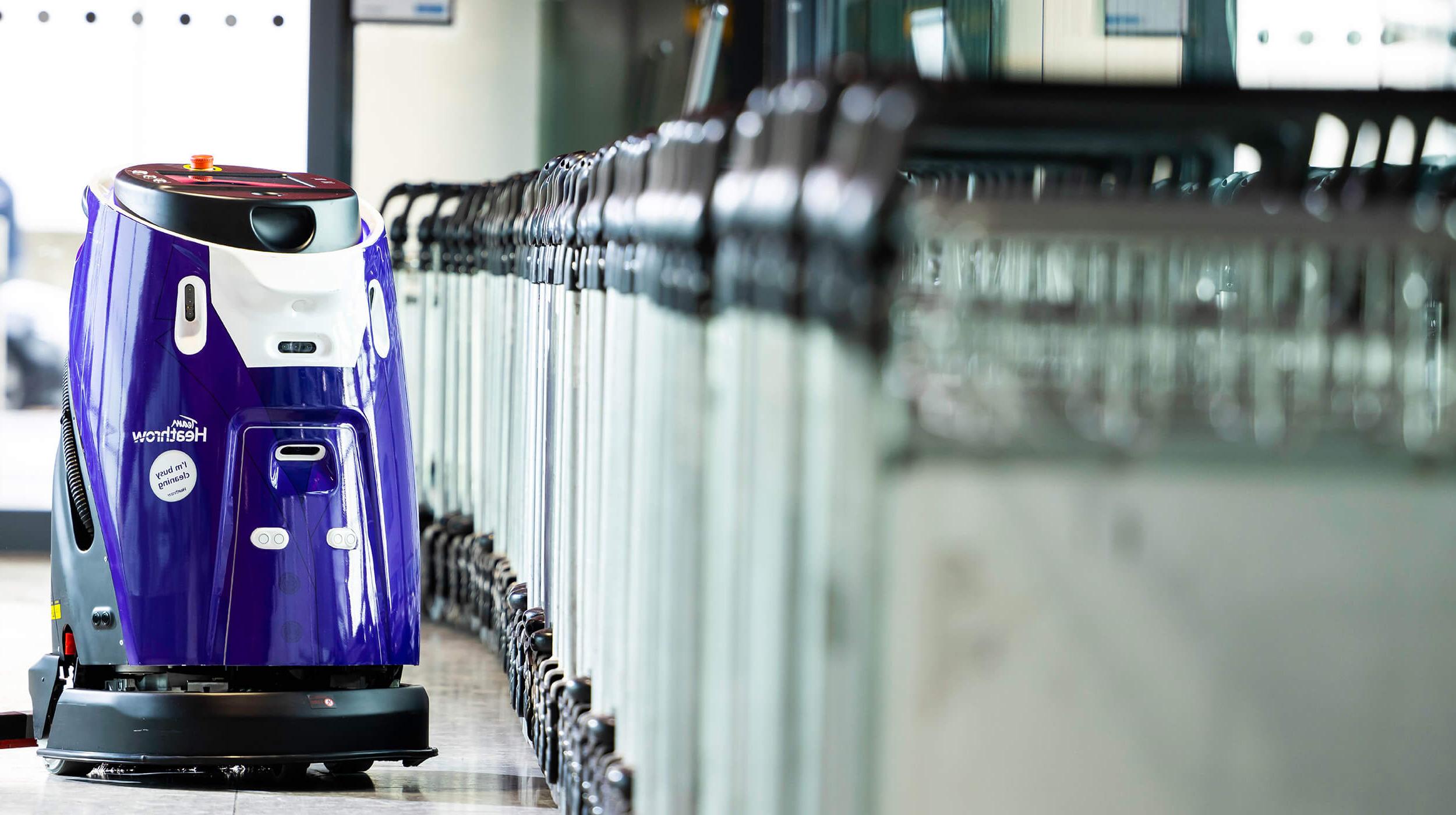 Mitie清洁机器人在伦敦希思罗机场，旁边是一排行李手推车